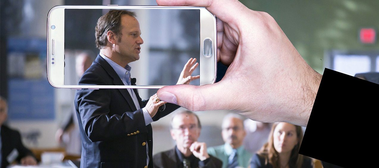 Social security and Medicare strategies with man speaking to crowd while someone takes a photo of him on a mobile phone..