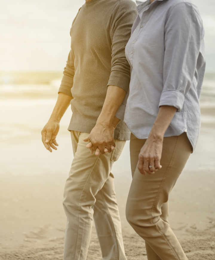 Retirement planning concept with older fit couple walking hand in hand on the beach.