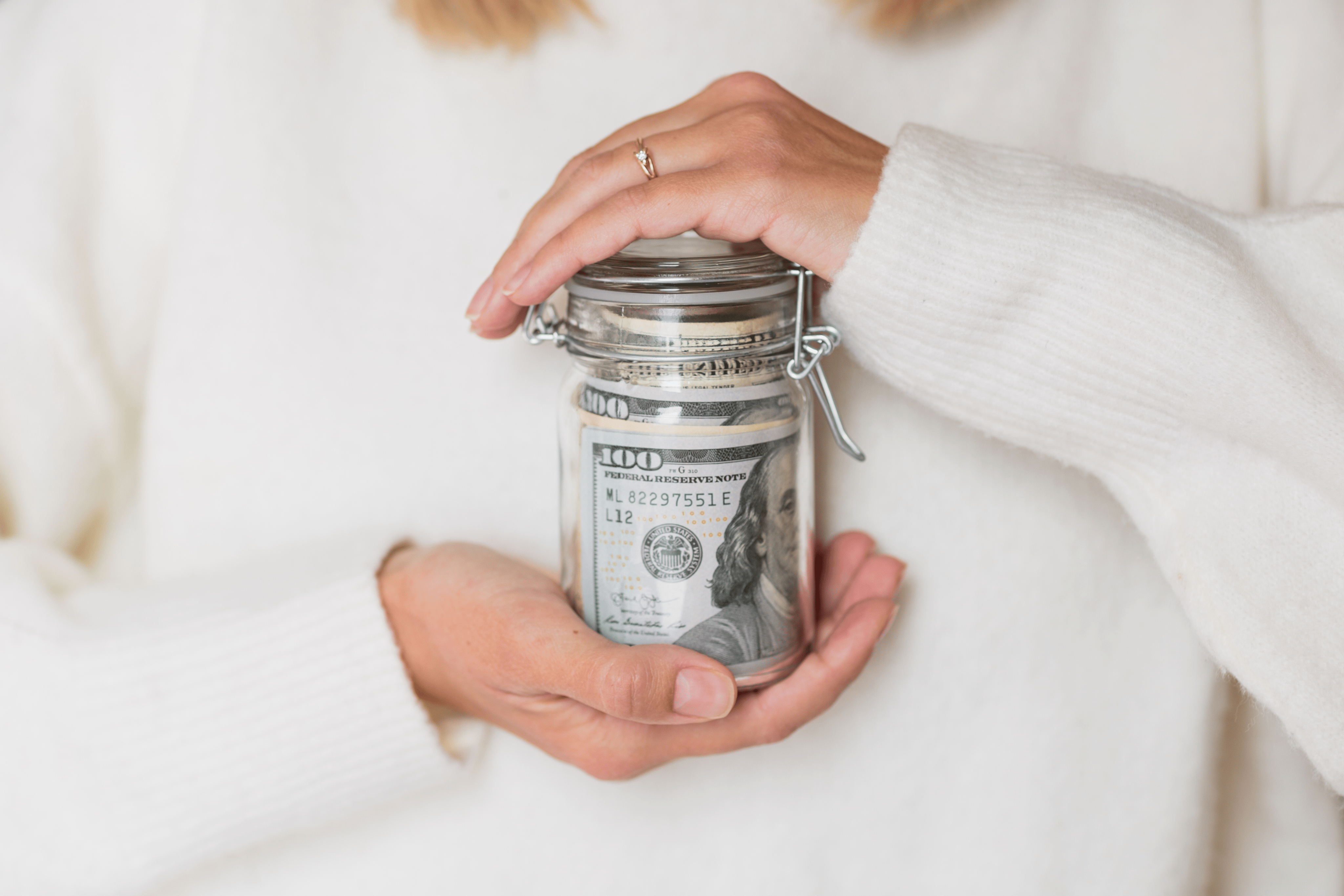 Wealth management concept with woman holding a glass jar with a roll of money inside.